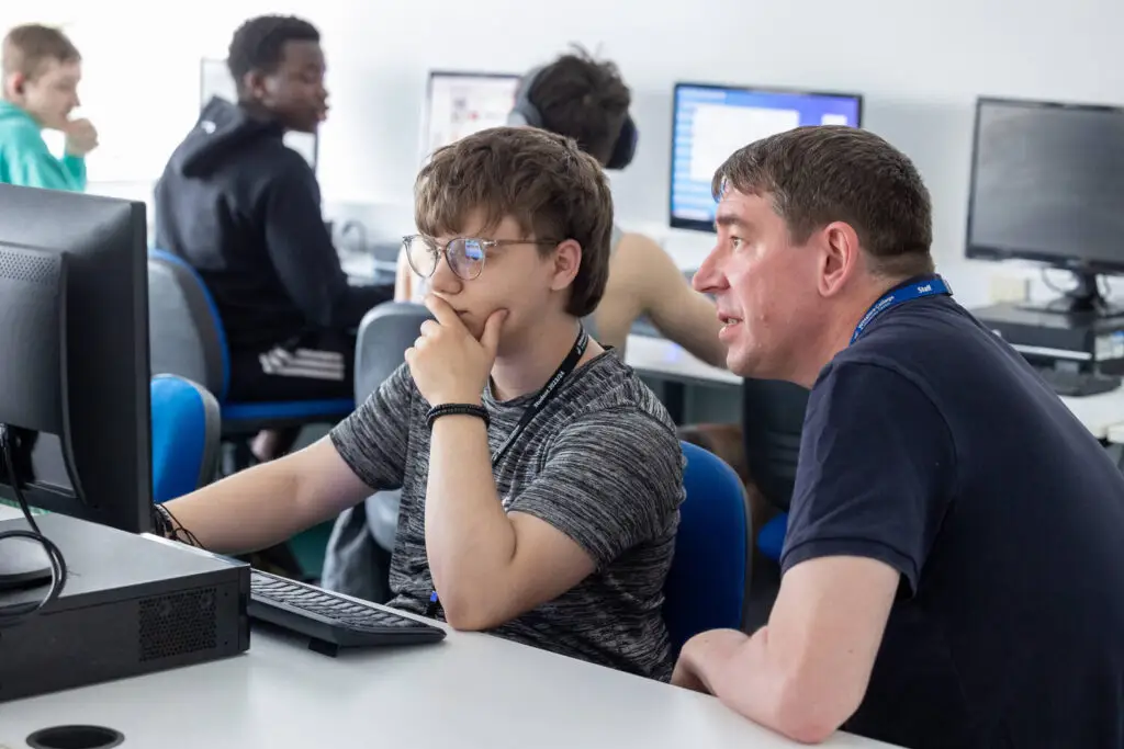 business student with teacher sat at a computer
