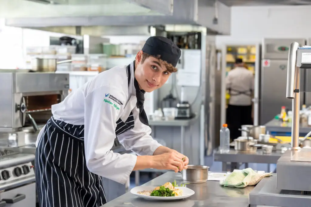 male catering student in kitchen plating up a meal