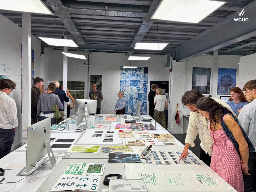 Visitors viewing graphic designer and art projects displayed on long tables during a student exhibition at Wiltshire College & University Centre's Trowbridge campus.