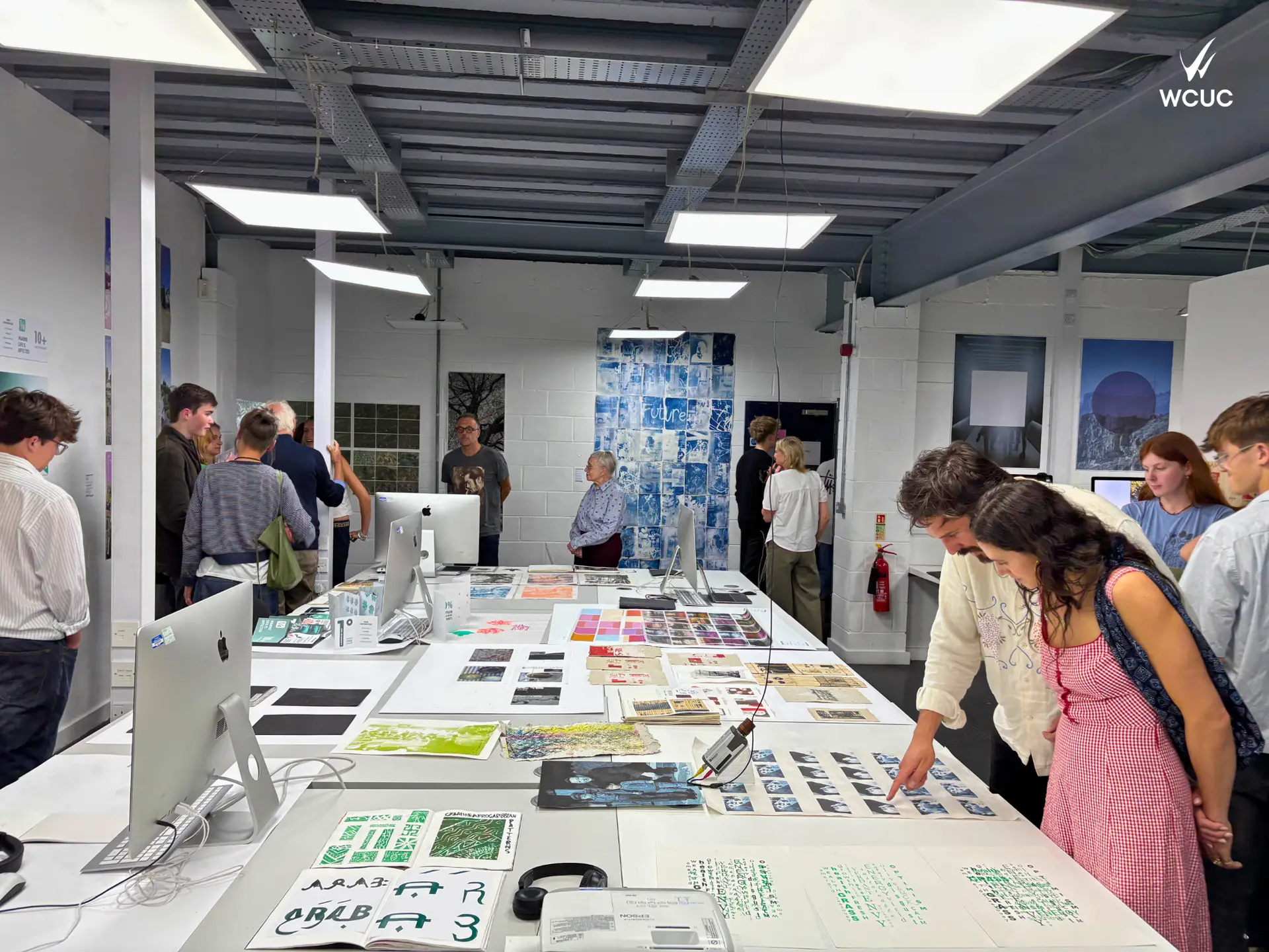 Visitors viewing graphic designer and art projects displayed on long tables during a student exhibition at Wiltshire College & University Centre's Trowbridge campus.