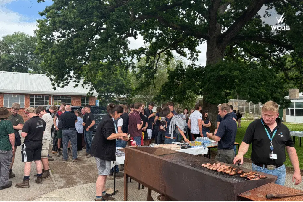 A lively BBQ scene with students and staff enjoying food and conversation under a large oak tree at Lackham.