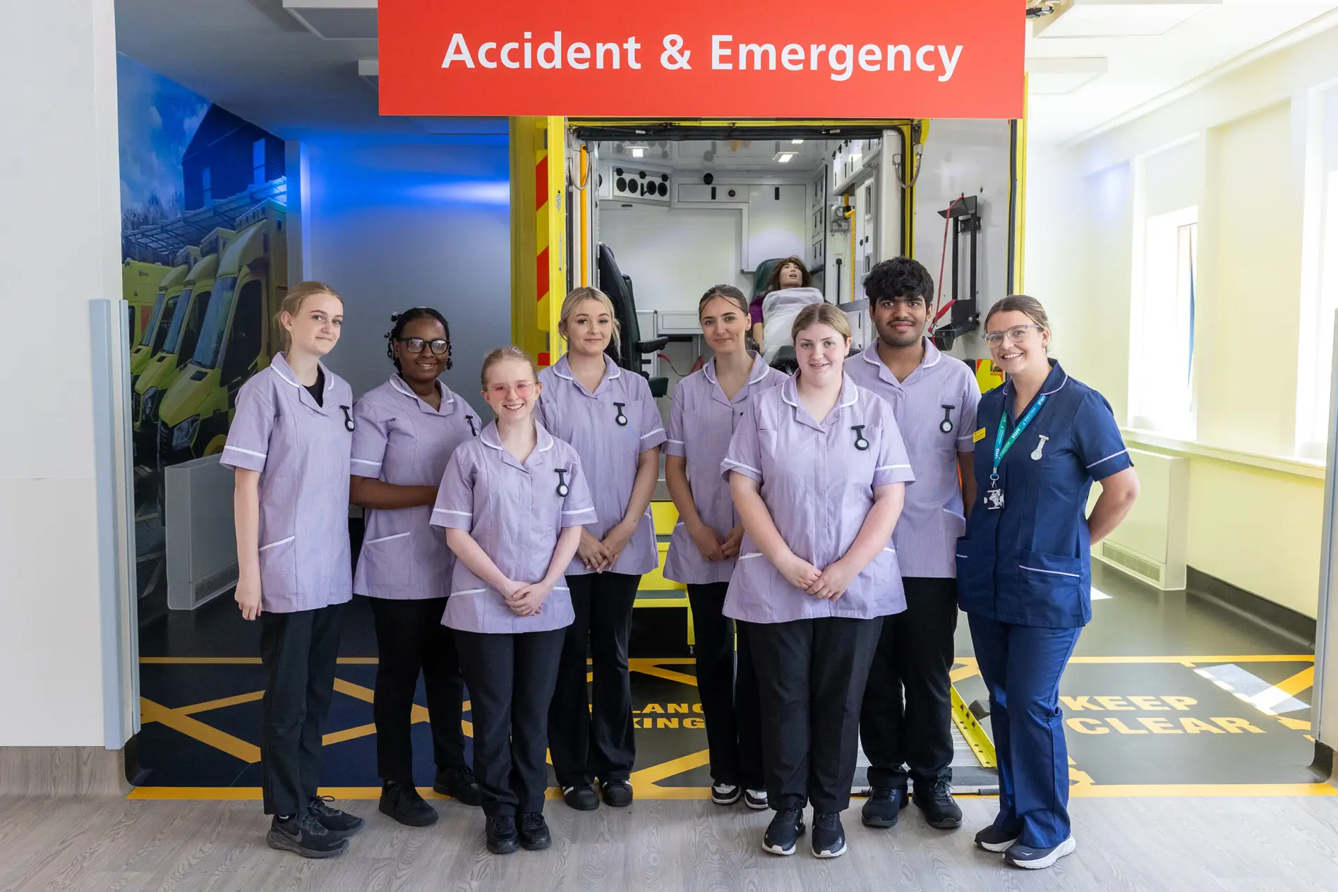 A group of student nurses and their tutor stand in front of a replica ambulance bay in the Health Care Zone's Accident & Emergency area.