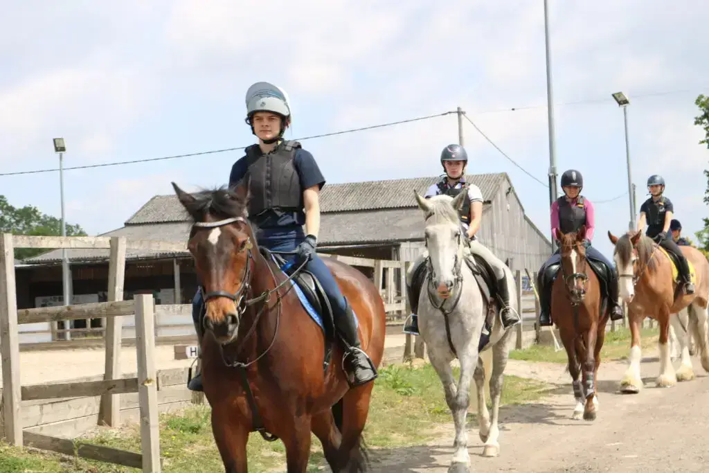 Group of equine students riding horses outdoors at Rein & Shine, wearing helmets and body protectors.
