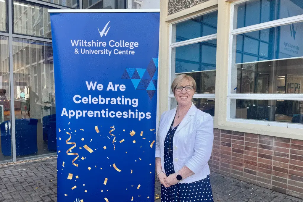 Janna Baker, Talent and Reward Manager at Meiyume, stands smiling beside a Wiltshire College & University Centre banner that reads ‘We Are Celebrating Apprenticeships’.