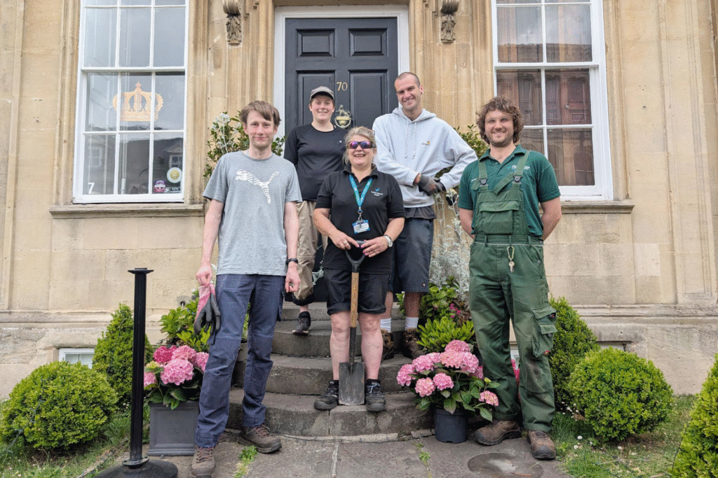 A group of horticulture staff and students from Wiltshire College & University Centre stand outside a Georgian building surrounded by newly planted flowers.