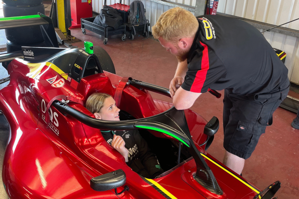 A female sat in a red Formula 4 car, talking to a man outside of the car.