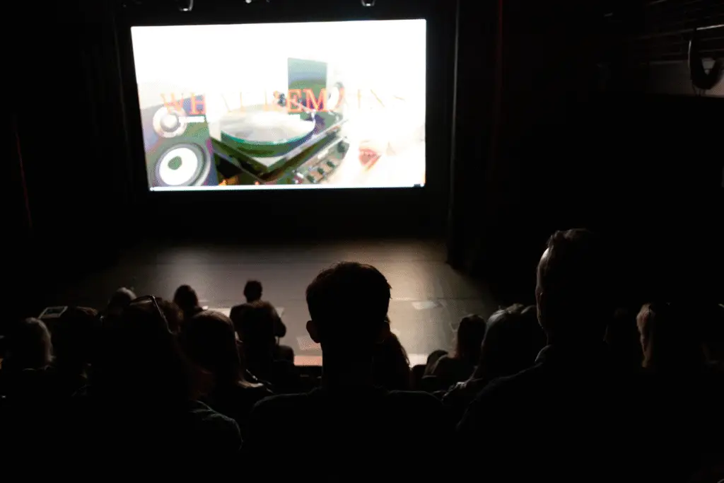 Audience silhouettes in front of a large cinema screen showing a student film.