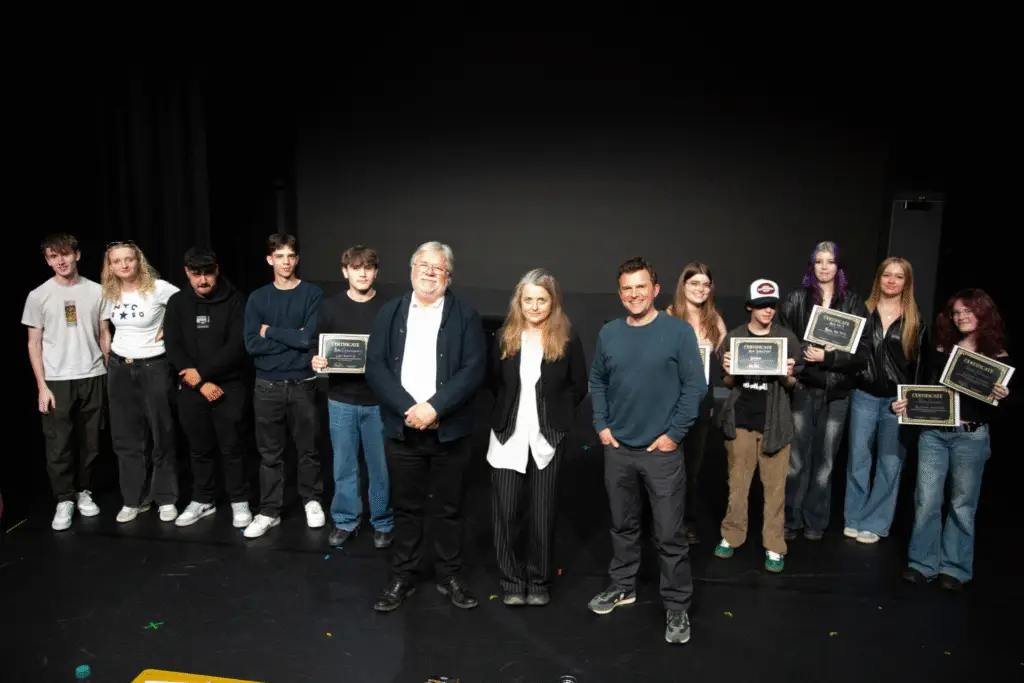 A group of students and judges stand on stage holding certificates.