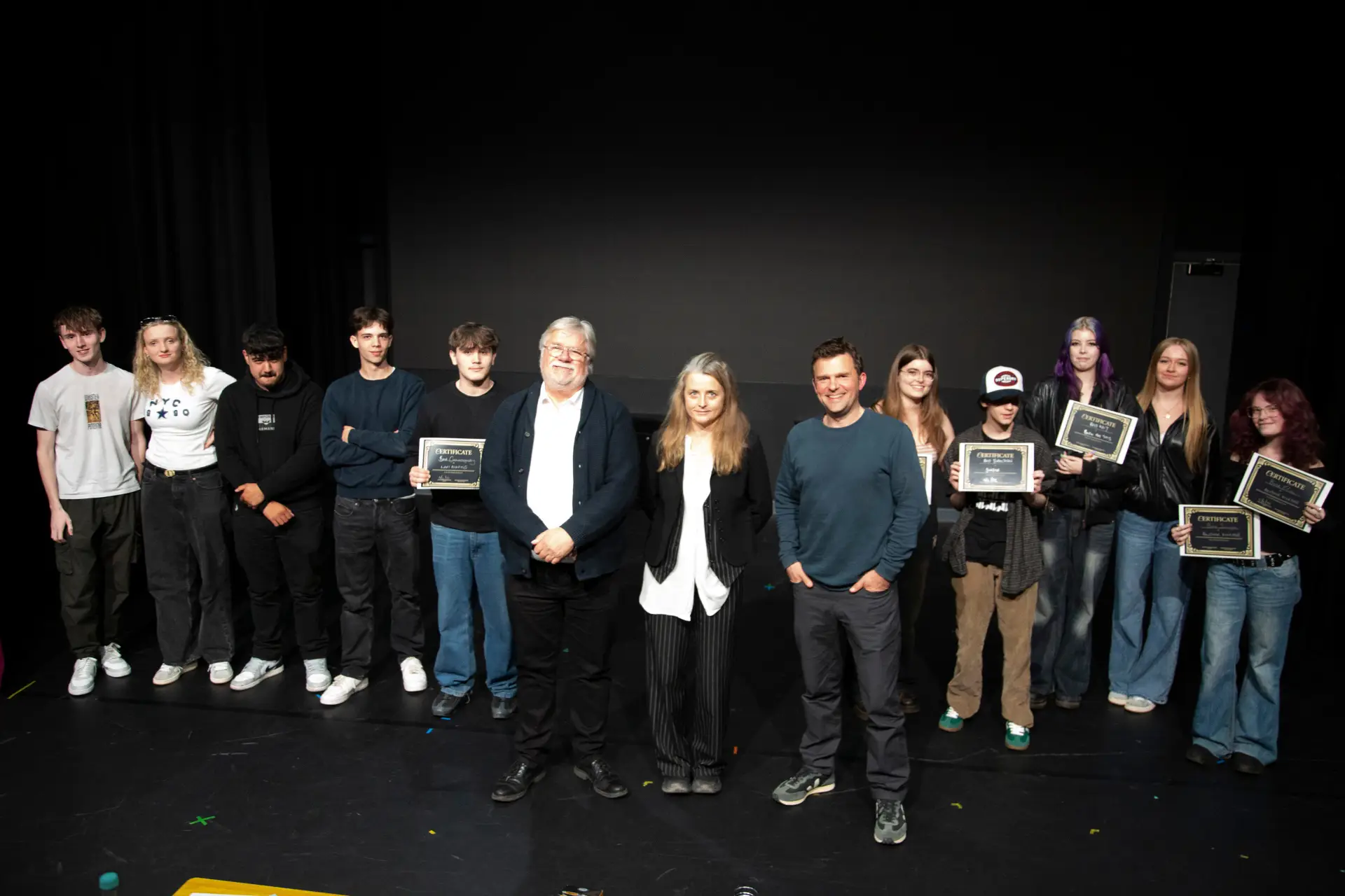 A group of students and judges stand on stage holding certificates.