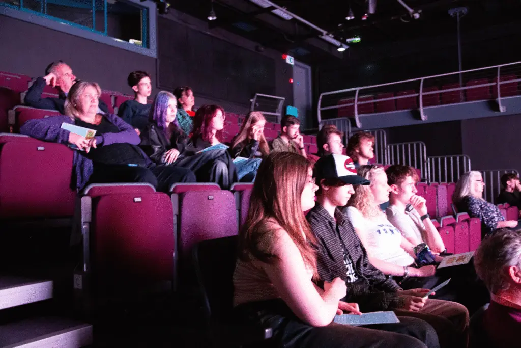 Audience members seated in theatre rows watching student films.