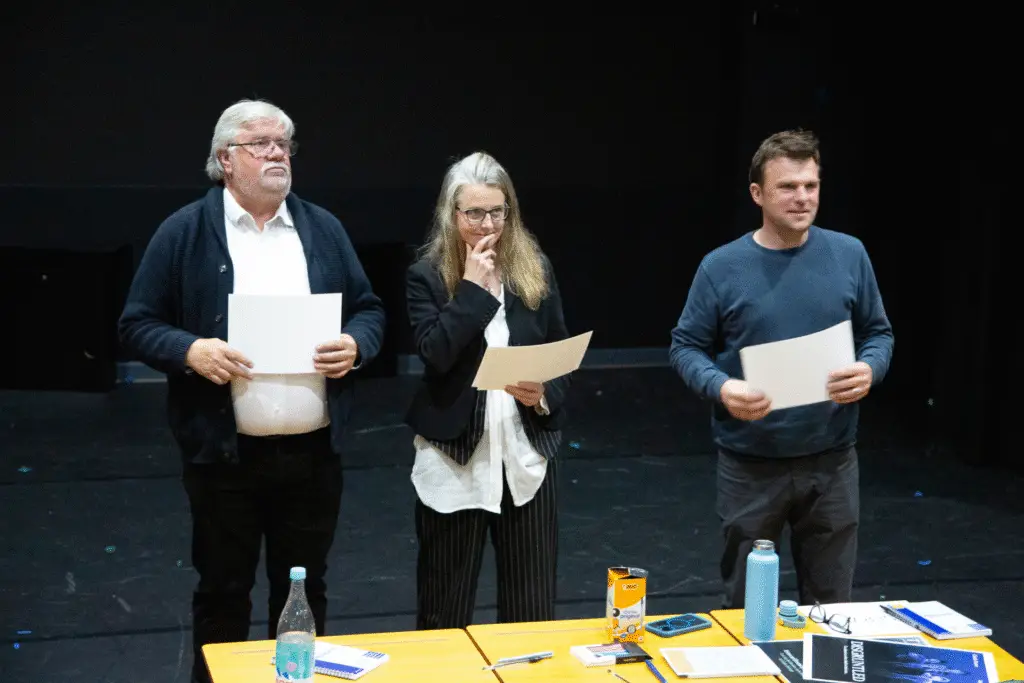 Three judges stand on stage holding certificates at the festival.
