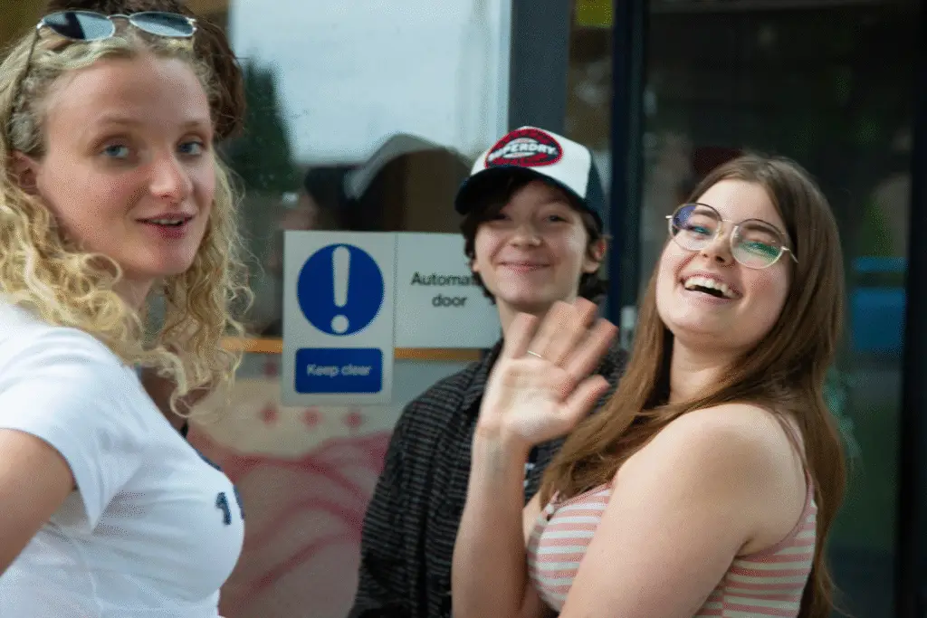 Three students smiling and waving outside the theatre entrance.