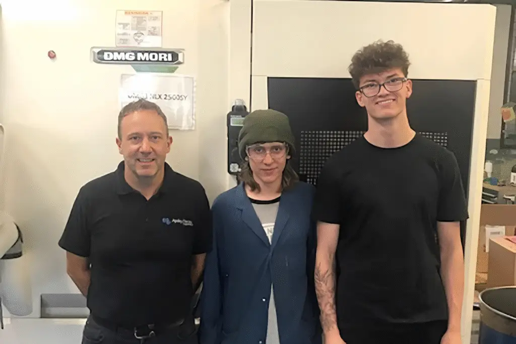Three people standing in front of engineering machinery at Apsley Precision Engineering, including a staff member and two students on T Level placements.