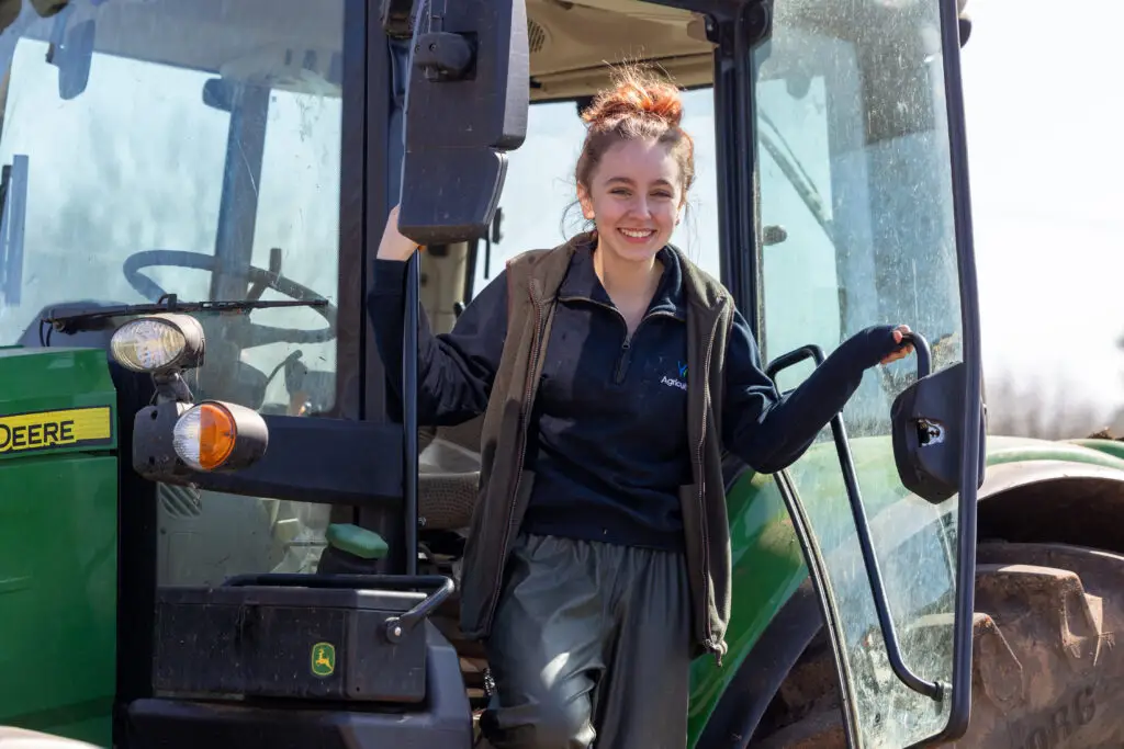 Student standing in the doorway of a green tractor at Lackham campus, smiling at the camera.
