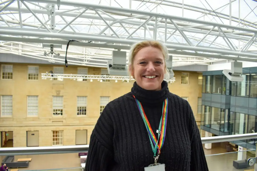 Spokesperson for Wiltshire Council smiling indoors at County Hall, wearing a rainbow lanyard.