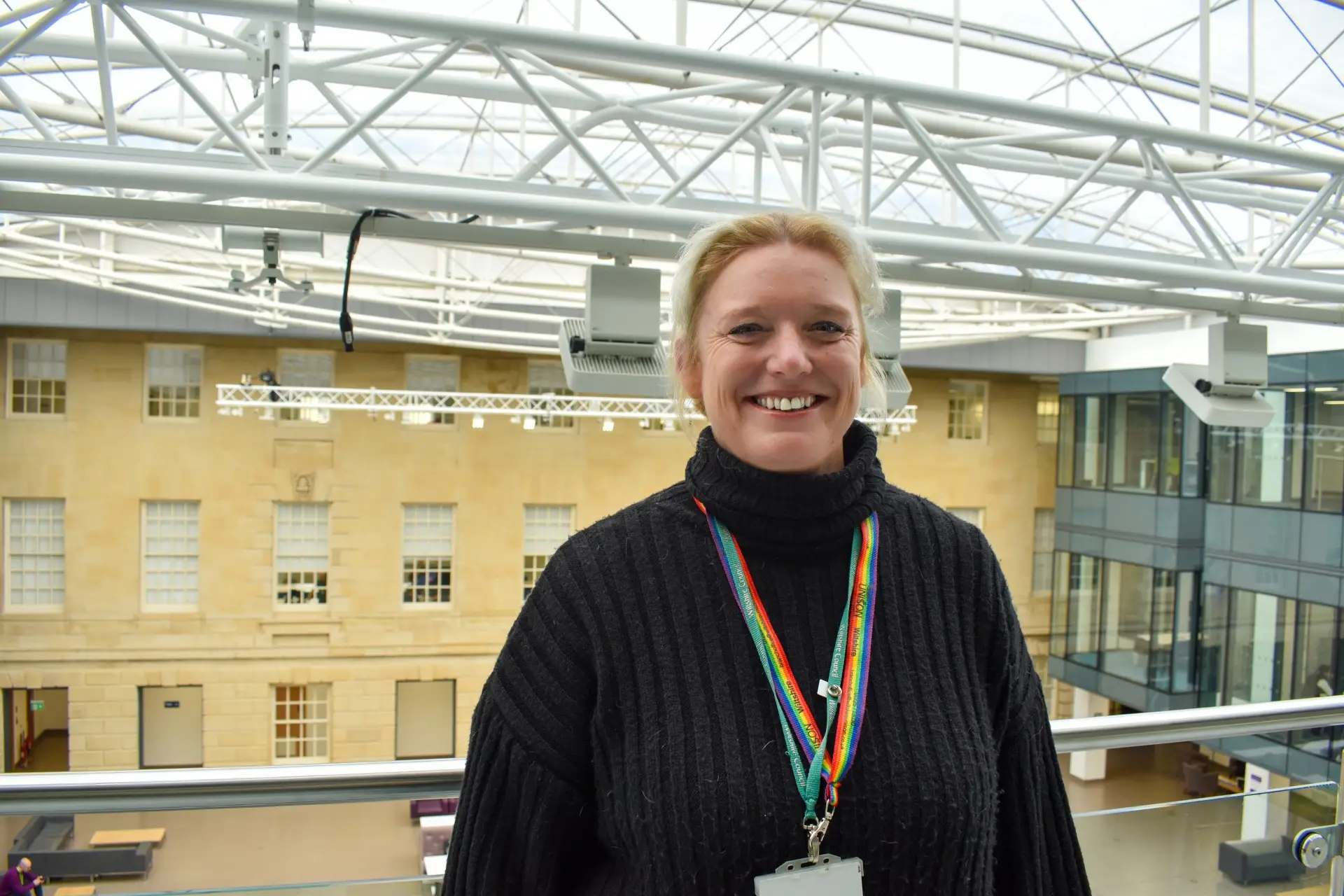 Spokesperson for Wiltshire Council smiling indoors at County Hall, wearing a rainbow lanyard.