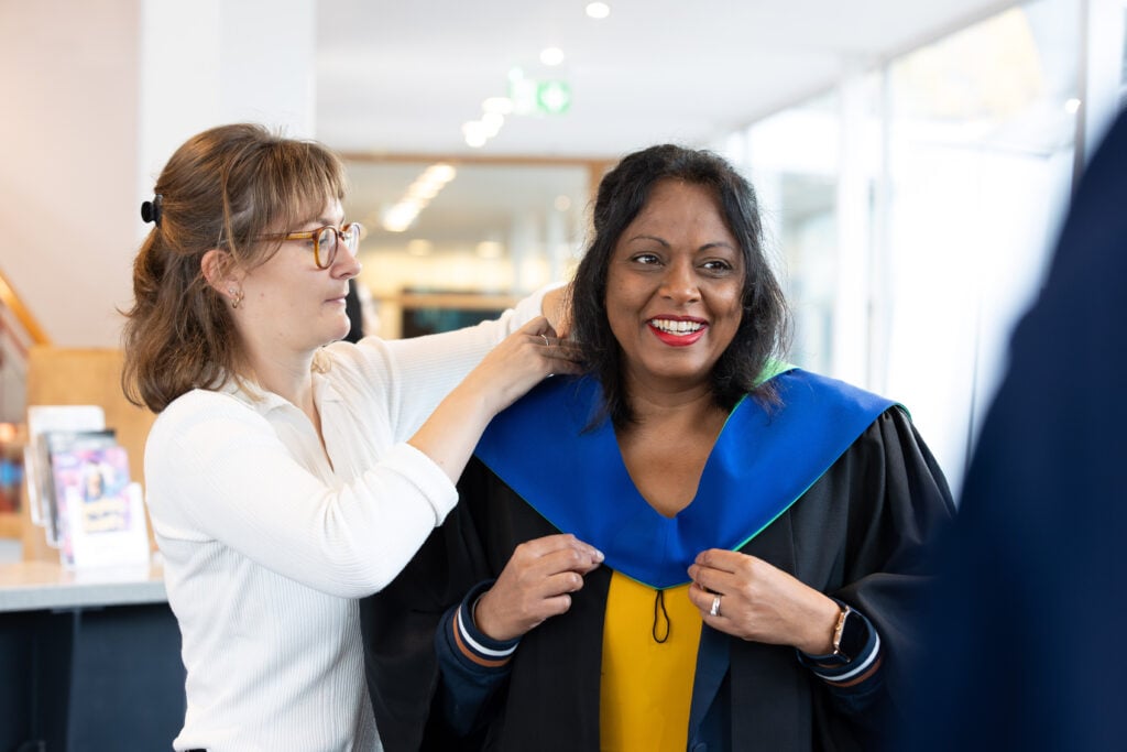 A higher education students getting help with her graduation robe.