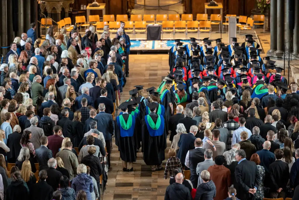 Inside Salisbury Cathedral - lots of guests standing at their seats and graduands walking in the centre.