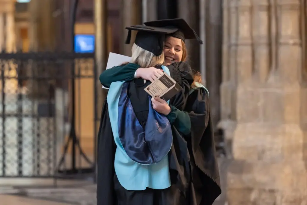 Two students graduating hugging each other.