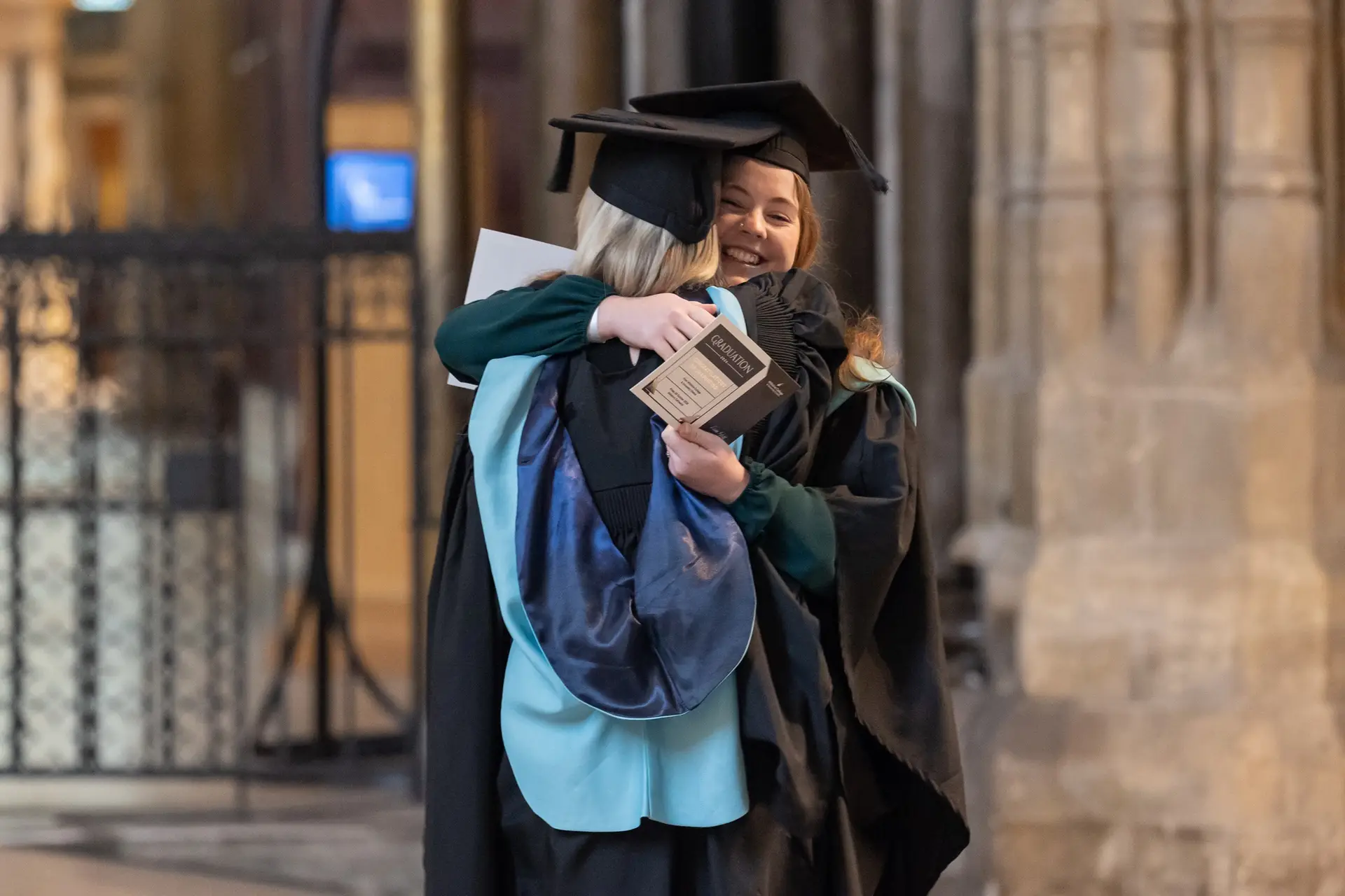 Two students graduating hugging each other.