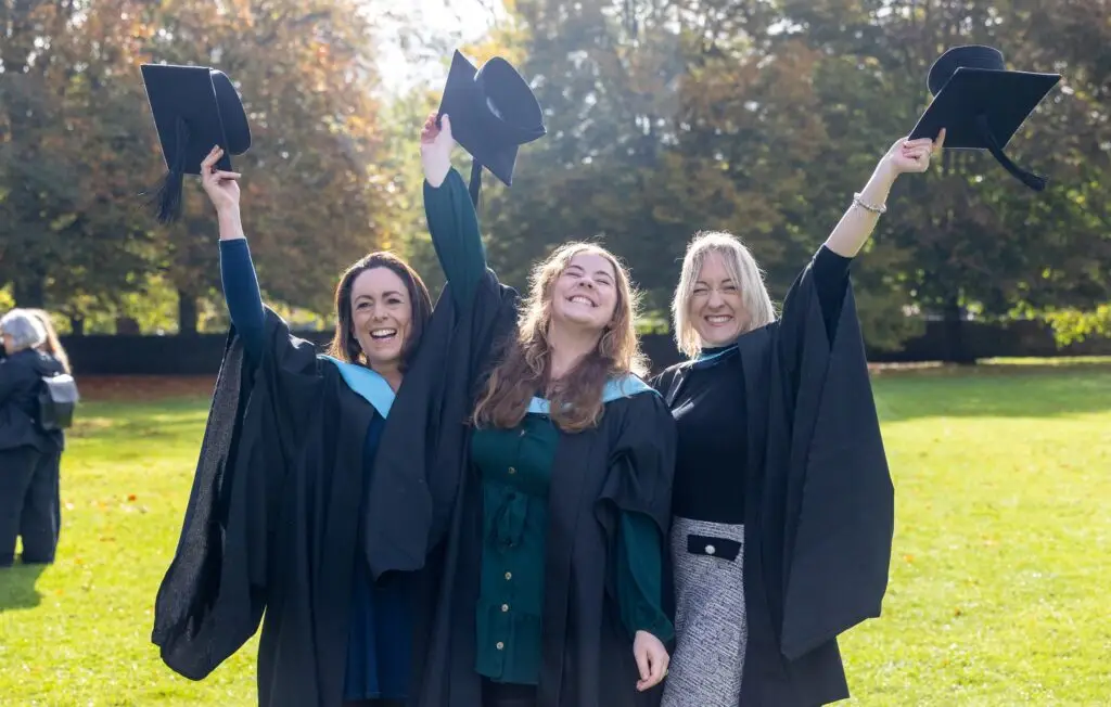 Three young women celebrating outside with their caps up in the air in their hands.