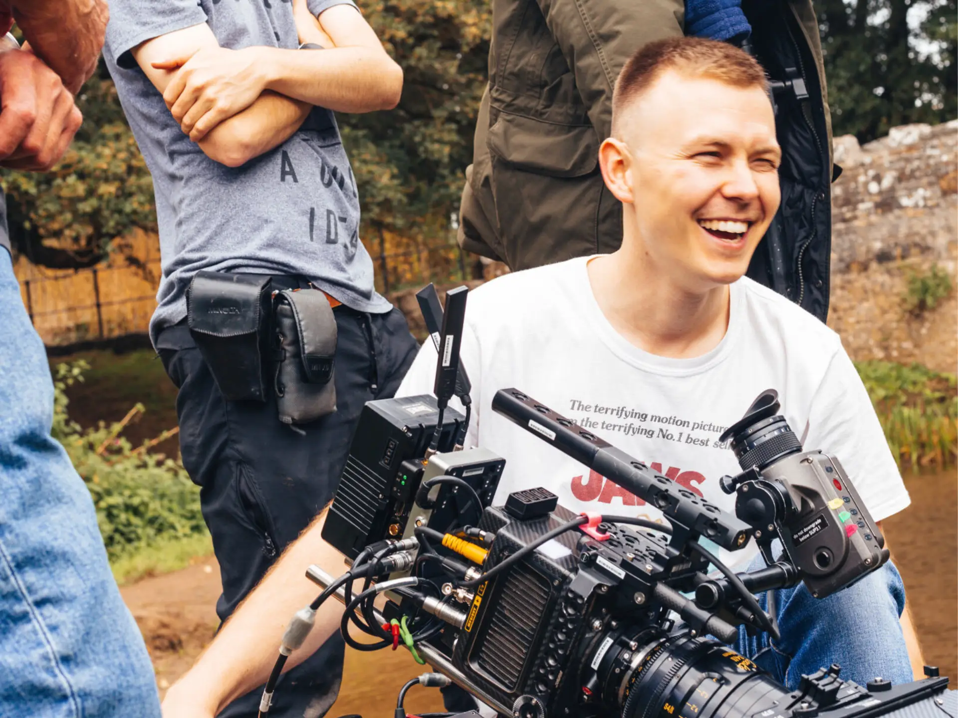 Student filmmaker laughing while operating a professional cinema camera during a film shoot outdoors.