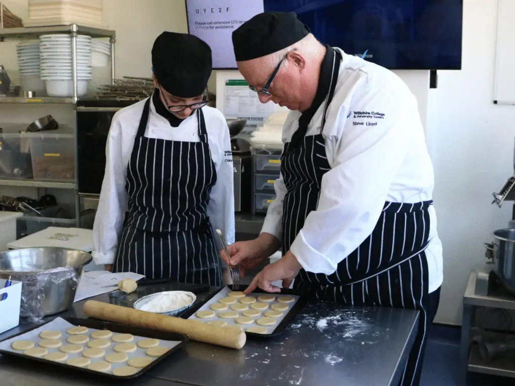 A chef lecturer guiding a hospitality student as they prepare food on a baking tray.