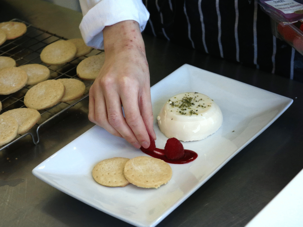 A student plating a dessert with raspberries and biscuits.
