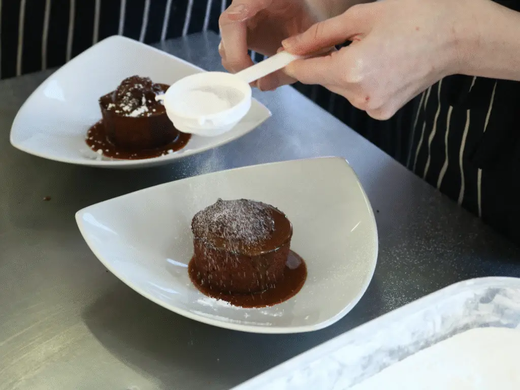 A hospitality student dusting icing sugar over a plated dessert in the training kitchen.