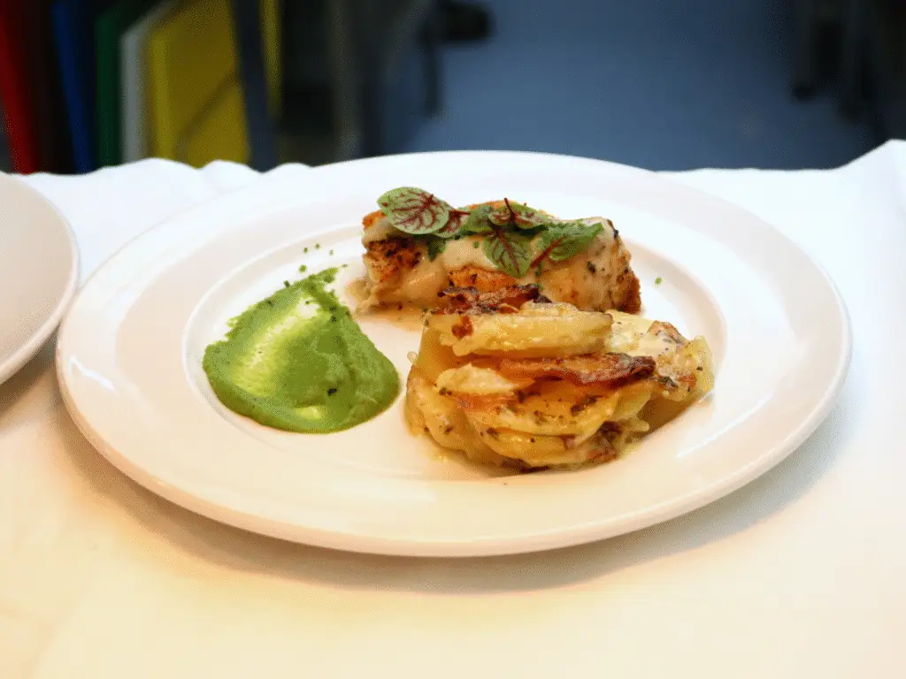A plated chicken dish served with potato gratin and green puree on a white plate.