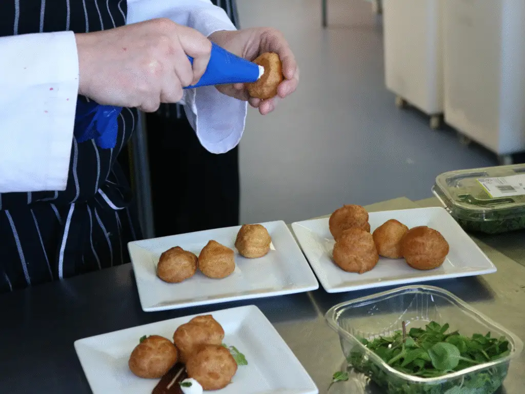 A hospitality student piping filling into savoury choux-style pastries during a kitchen session.