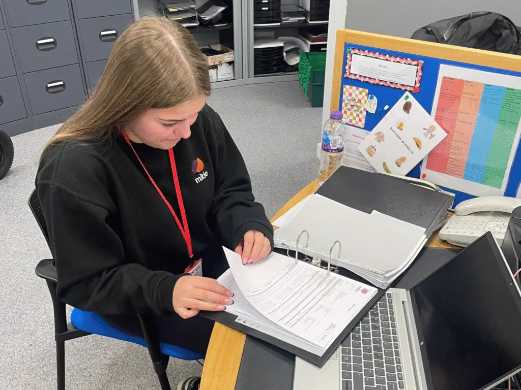 A female student sat at a desk with a folder.