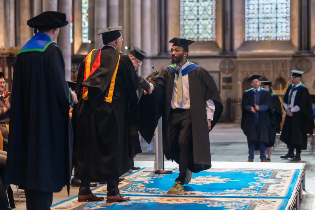 Higher education student walking across the stage and shaking hands with lecturer.