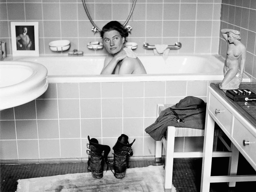 Lee Miller sitting in Adolf Hitler’s bathtub in his Munich apartment in 1945, with her muddy army boots placed on the bath mat in front of her.