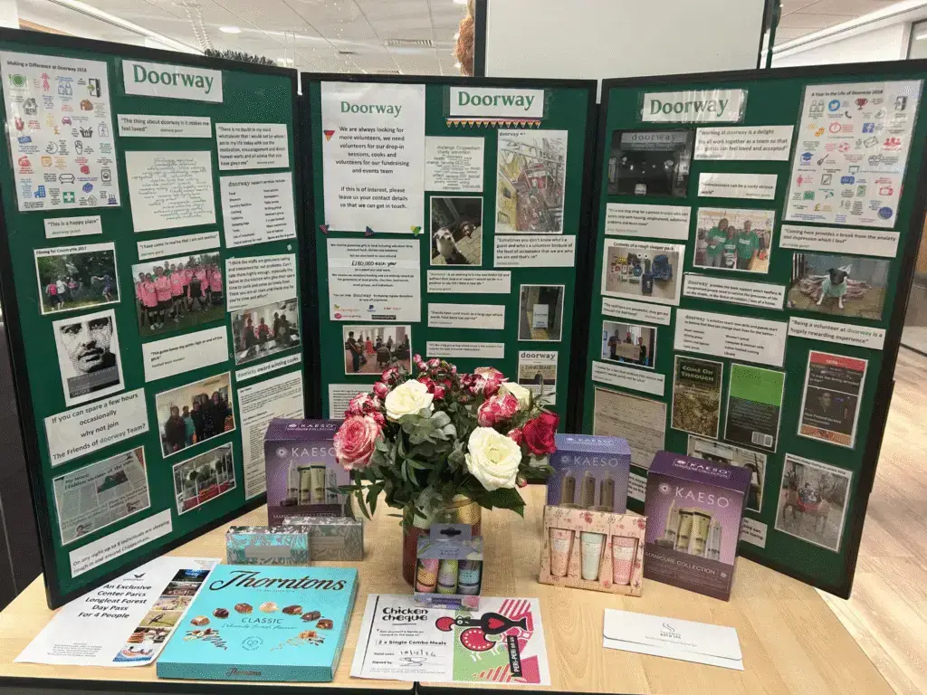 Doorway charity information boards displayed on a table with raffle prizes, including beauty products and chocolates.