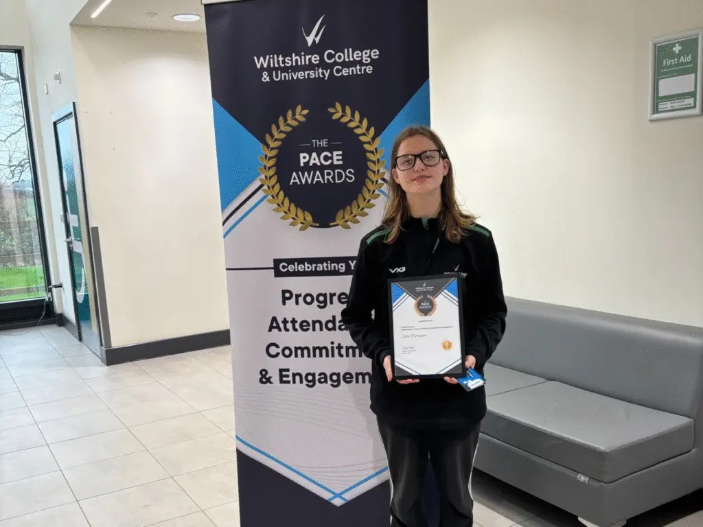 A student holding a PACE Award certificate stands in front of a Wiltshire College & University Centre PACE Awards banner.