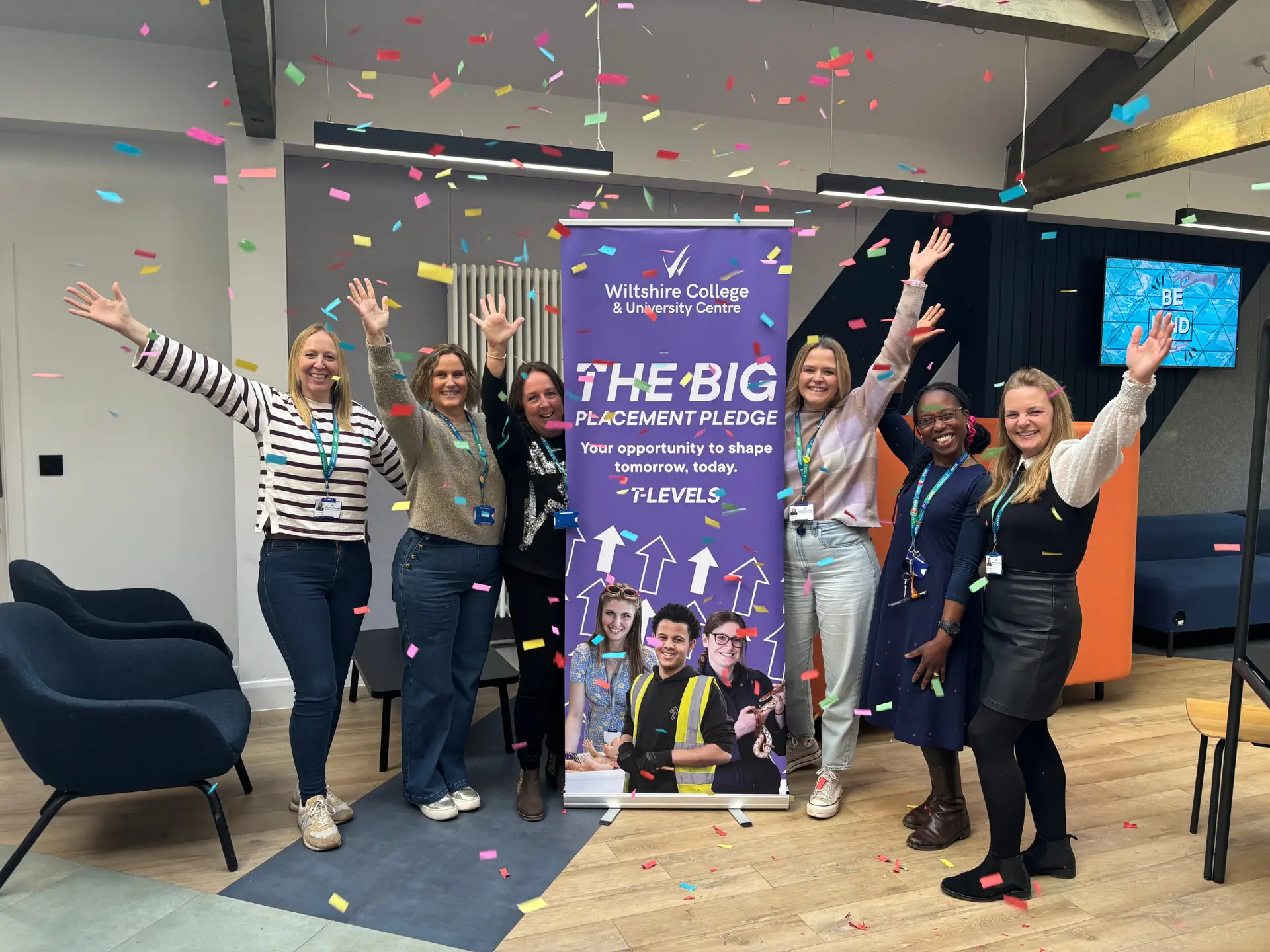 A group of staff from Wiltshire College & University Centre’s Work Placement Team stand in front of a BIG Placement Pledge banner with their arms raised as colourful confetti falls around them.