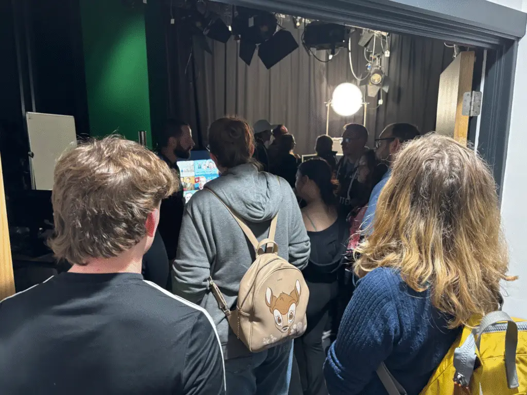 A group of visitors gathered inside a college media studio listening to a tutor speak.