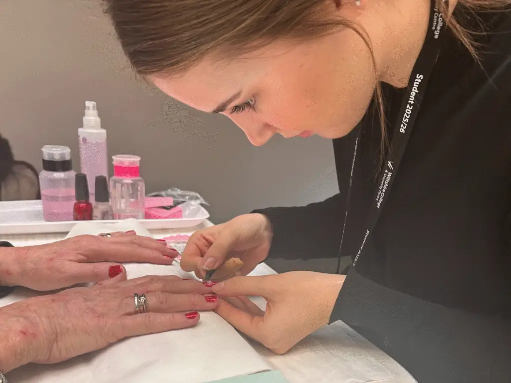 A Hair and Beauty student applying red nail polish during a festive nail treatment.