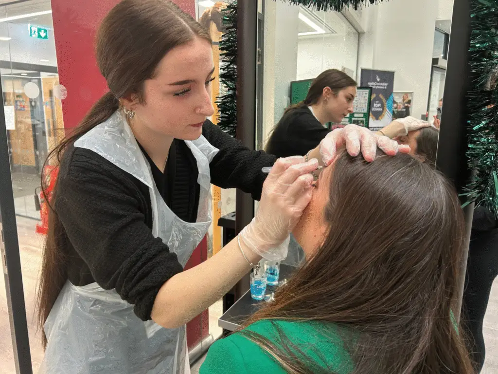 A Hair and Beauty student carrying out an eyebrow treatment while wearing protective gloves.
