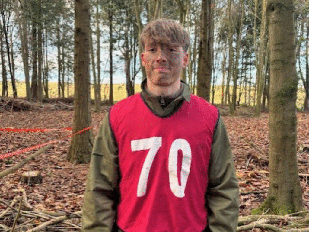 A student wearing a numbered training bib stands outdoors in woodland.
