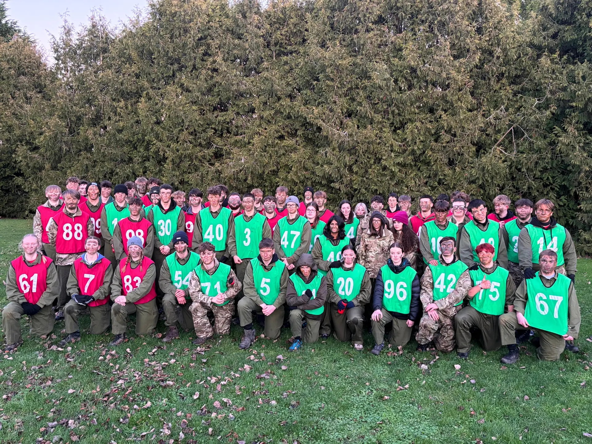 Large group of students wearing numbered training bibs pose together outdoors.