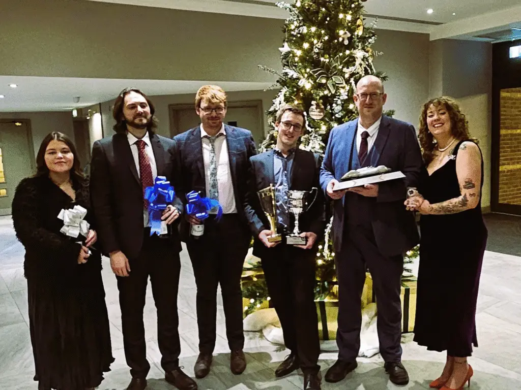 The WCUC Motorsport team standing together at the Castle Combe Racing Club Awards, holding prizes and posing beside a decorated Christmas tree.