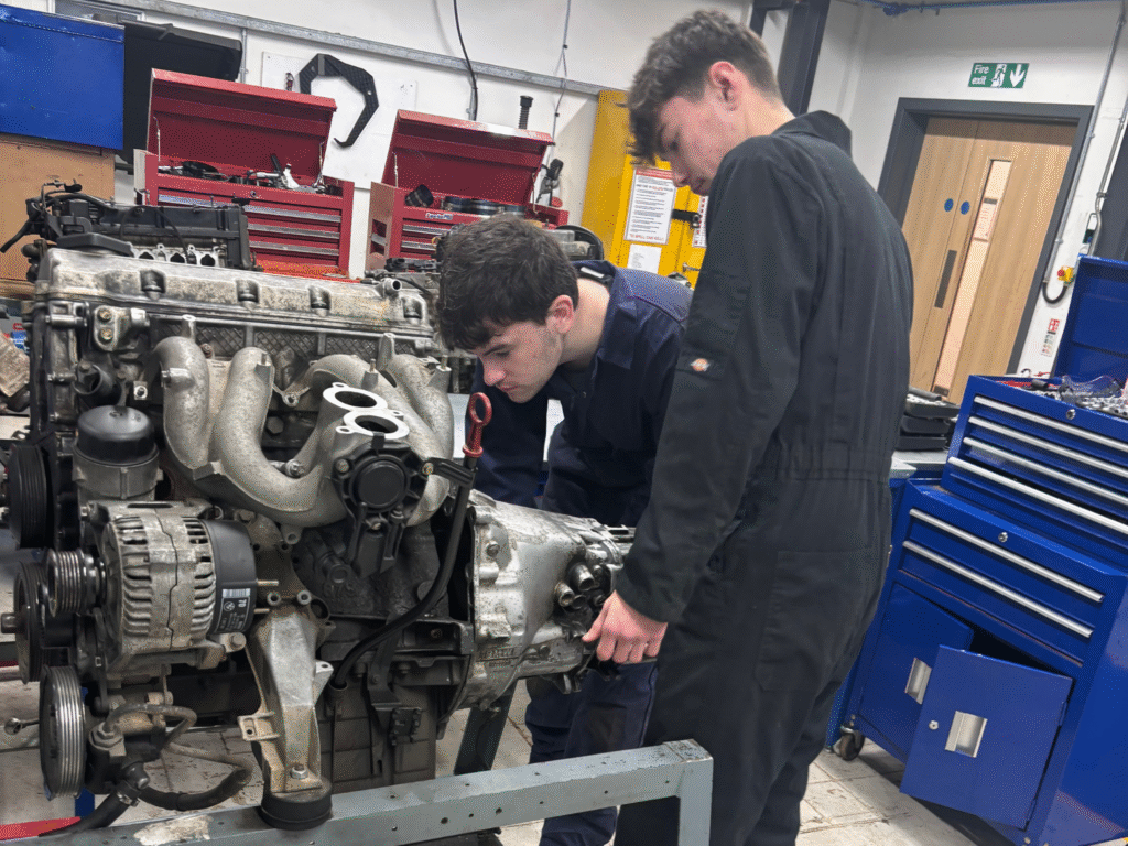 Automotive students working together on an engine rig during a practical skills task.