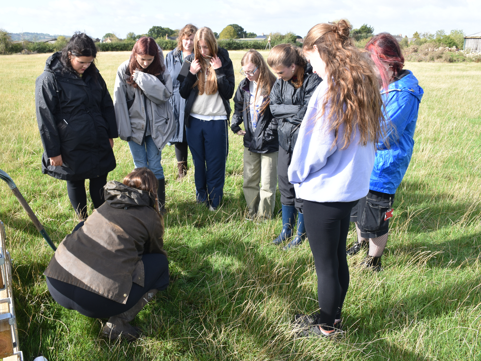 Students gather around a soil sampling demonstration in a grassy field.