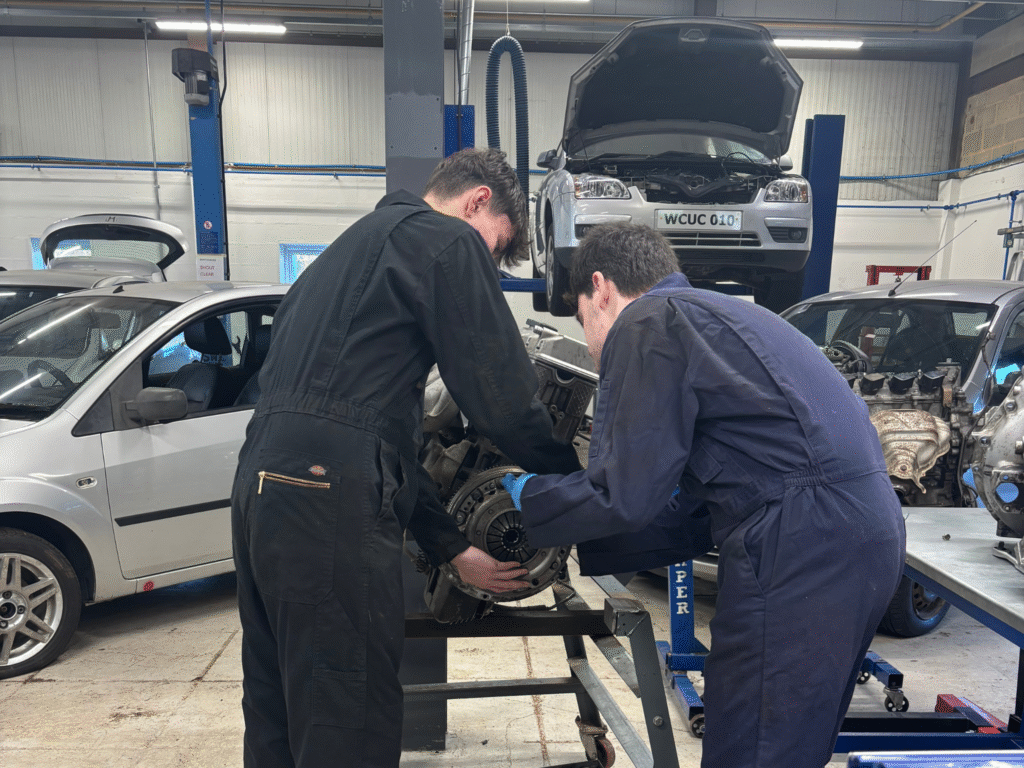 Two automotive students fitting a clutch to an engine rig in a workshop.
