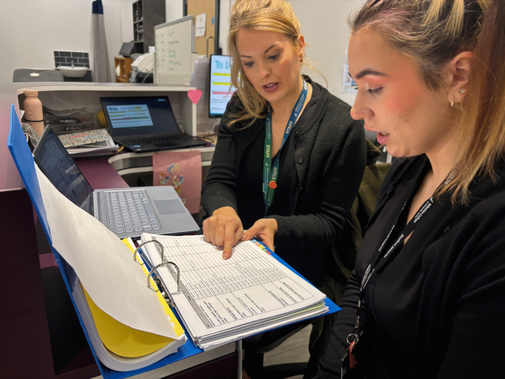A lecturer and a student sit together during a tutorial, reviewing a progress document and discussing next steps.