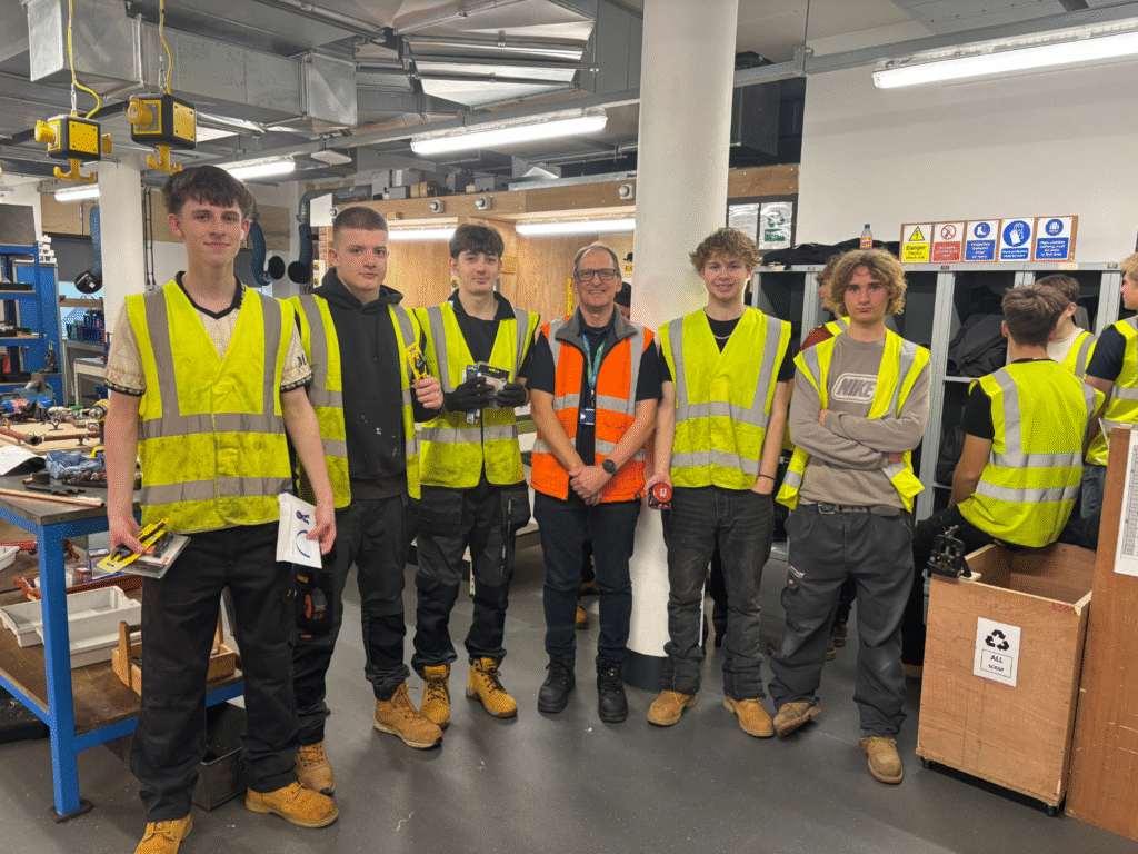 Group of Level 1 Plumbing students wearing high-visibility vests standing in a workshop at the Chippenham campus following a plumbing competition.