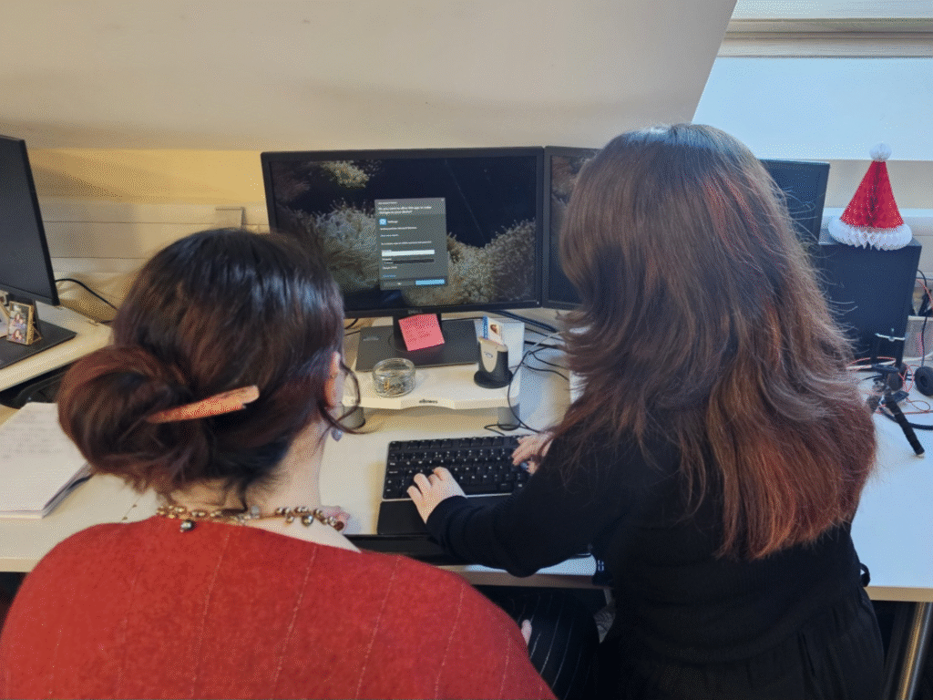 An ICT apprentice working with a colleague at a computer workstation.