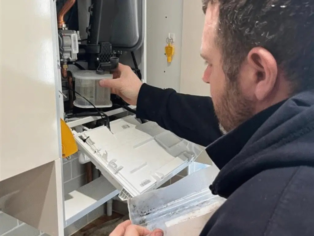 Plumbing apprentice removing a condensate trap from inside a boiler unit.